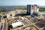An aerial view of Launch Complex 39 shows the south and west sides of the Vehicle Assembly Building. The curved roadway heading to the VAB leads to the high bay 2, the Safe Haven facility constructed in 2000. The white building in the foreground is the Processing Control Center. Beyond it is the Orbiter Processing Facility, bays 1 and 2. The OPF bay 3 is farther still, closer to the VAB. Farther in the background are the waters of Banana Creek in the Merritt Island National Wildlife Refuge.